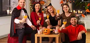 Group of friends in Halloween costumes, smiling and holding drinks at a festive gathering.