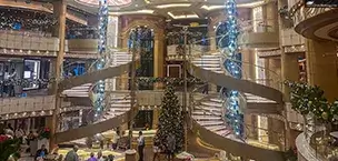 Elegant cruise ship atrium decorated for Christmas with grand staircase and blue chandelier.