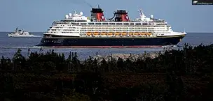 Disney Magic cruise ship sailing near a rocky coastline under clear skies