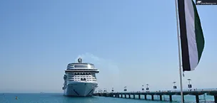 Cruise ship docked at a port in Dubai with the UAE flag flying high in the foreground.