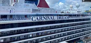 Carnival Dream cruise ship with iconic red, white, and blue funnels against a cloudy sky.