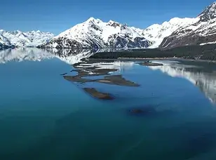 A snow-capped mountain reflected in a calm lake, with a clear blue sky above.