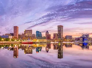 Baltimore, Maryland skyline at dusk. The image showcases the city's illuminated skyscrapers, with the Inner Harbor reflecting the lights in the water.