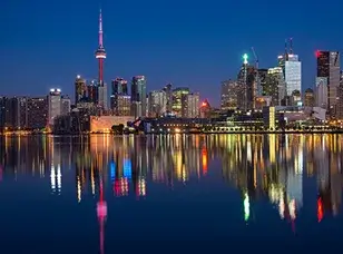 A panoramic view of the Toronto skyline at night, showcasing the illuminated CN Tower and a cluster of skyscrapers along the waterfront.