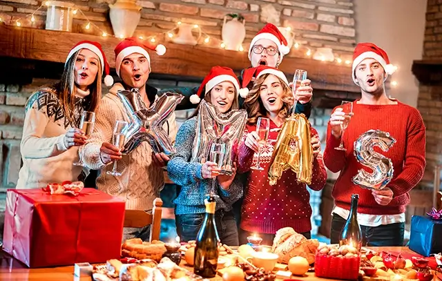 A group of friends celebrates Christmas with champagne and sweet food at a dinner party with Santa hats