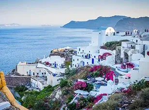 A picturesque view of Oia, Santorini, Greece, featuring whitewashed buildings, iconic blue-domed churches, and the Aegean Sea in the distance.