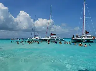 A group of people interacting with a large group of stingrays in shallow, clear turquoise water.