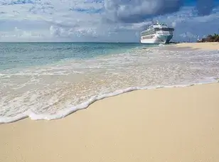 A large cruise ship docked at a pier in Grand Turk Island. The ship is surrounded by clear turquoise water and a white sandy beach.