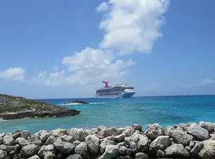 Carnival Splendor cruise ship docked at a port. The image shows the large white vessel with its distinctive red funnel, surrounded by water and other ships in the background.