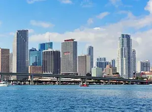 A panoramic view of the Miami skyline at sunset, showcasing tall skyscrapers reflecting in the calm water.