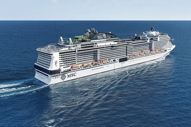 The MSC Grandiosa cruise ship sailing on a calm ocean under a clear blue sky, with multiple decks and outdoor areas visible on the top of the vessel.