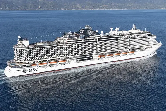 The MSC Seaside cruise ship sailing through blue waters with a distant coastline and mountains under a bright, clear sky.