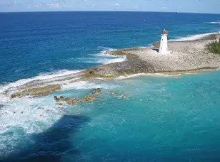 A white lighthouse stands tall on a rocky coastline, overlooking turquoise waters and a clear blue sky.