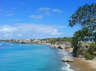 Aerial view of Playa Forti, Curacao, showcasing its turquoise water, rocky coastline, and a small beach with sunbathers.