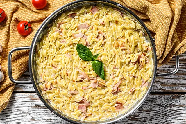 Italian pasta Orzo. Cream sauce recipe with bacon and basil. Preparation of risoni. Background made of white wood
