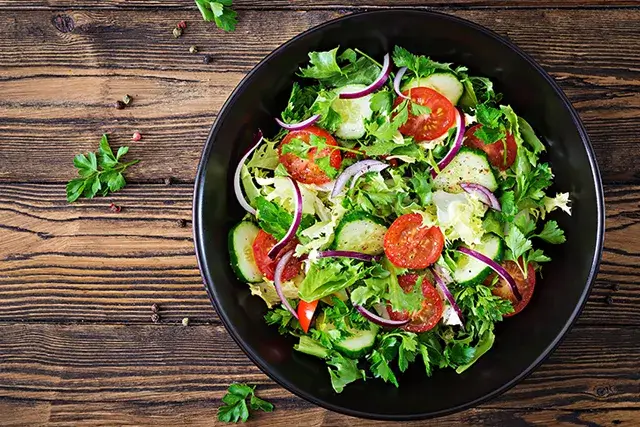 Salad made with tomatoes, cucumbers, red onions, and lettuce leaves. A healthy vitamin menu for summer. Vegetarian food that is vegan. Dinner table for vegetarians